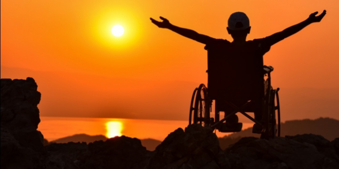 Silhouette of human figure with raised hands toward orange sunset over water