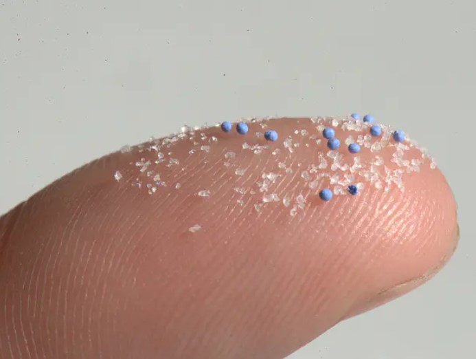 Photo of a finger tip with tiny, colorful pieces and beads of plastic.