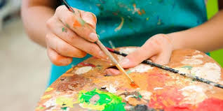 Persons hands holding a paint brush to mix colors on a paint palette