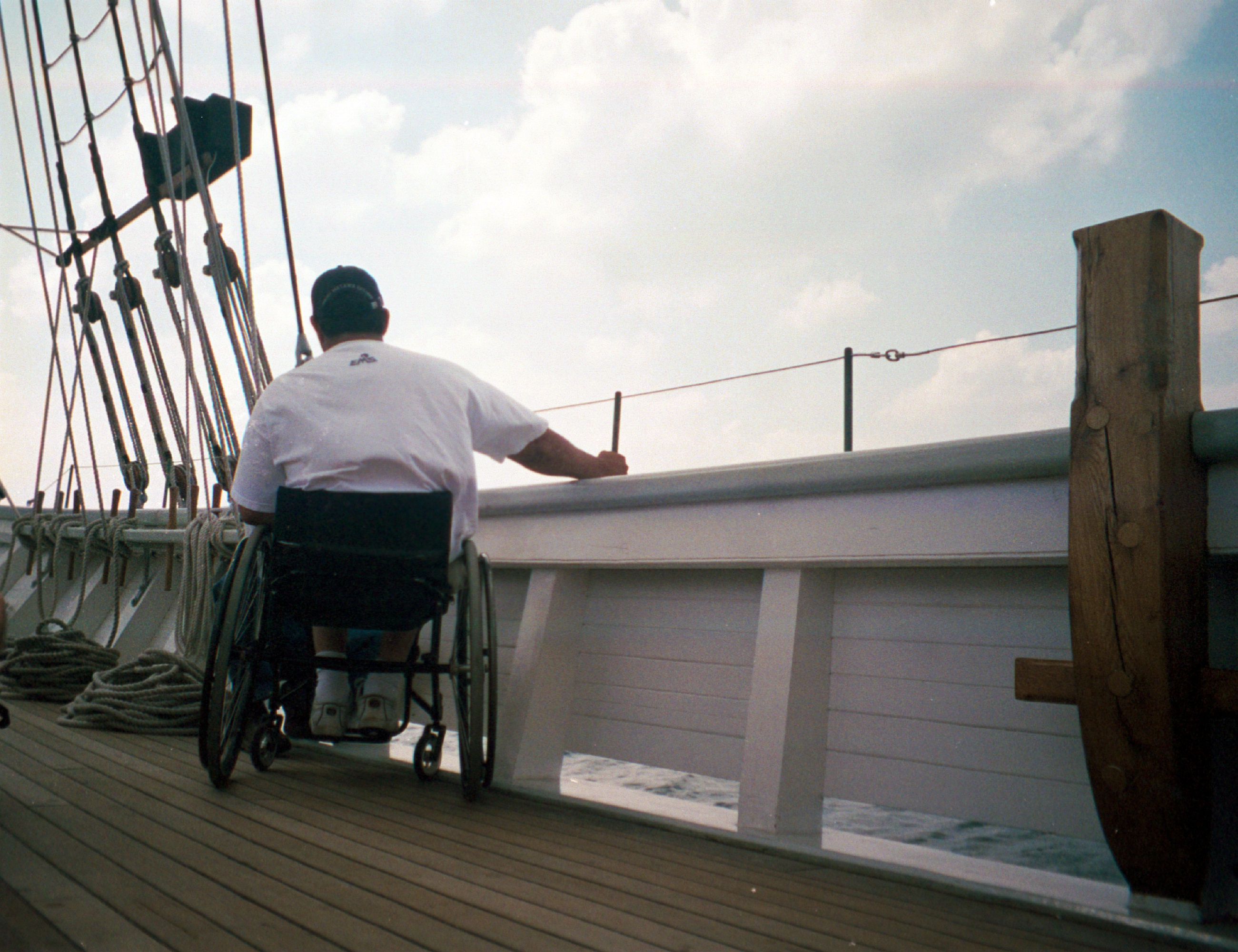 Person in a wheel chair holding on to the bow of a sailing vessel looking out