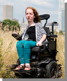 Emily, New NHU Staff member, sitting in her wheelchair in a tall grass field with city skyline in background.